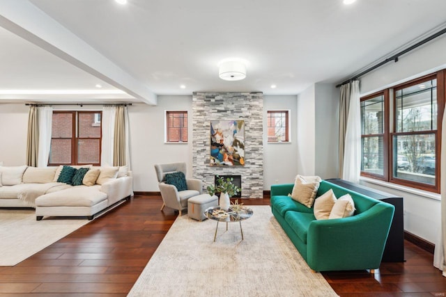 living area with a stone fireplace, dark wood-style flooring, and baseboards