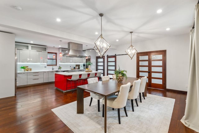 dining space featuring a barn door, dark wood-type flooring, and recessed lighting