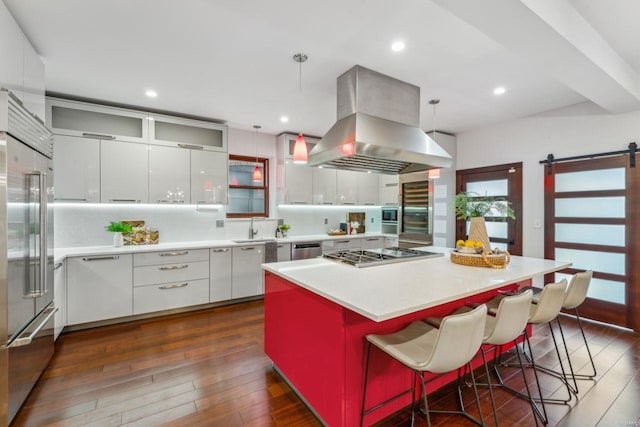 kitchen with stainless steel appliances, hanging light fixtures, a barn door, white cabinets, and island range hood