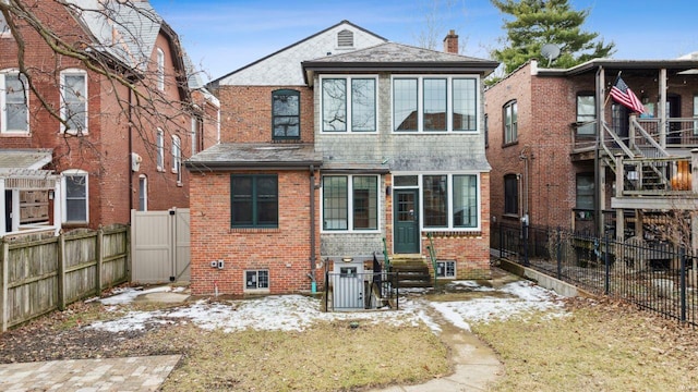 snow covered property with entry steps, brick siding, and a fenced backyard