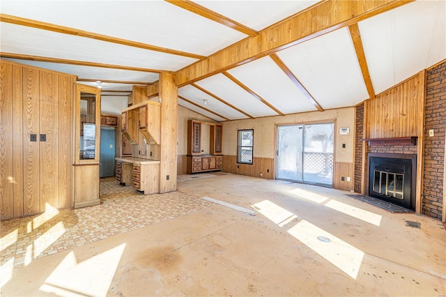 unfurnished living room featuring a fireplace, wooden walls, and vaulted ceiling with beams