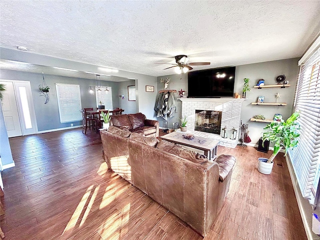 living room featuring ceiling fan, a fireplace, a textured ceiling, and hardwood / wood-style flooring