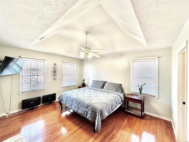 bedroom featuring a textured ceiling, ceiling fan, hardwood / wood-style flooring, and a tray ceiling