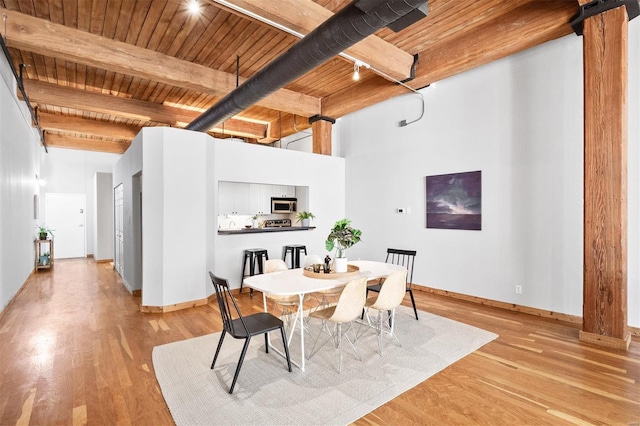 dining area with beam ceiling, light wood-type flooring, wooden ceiling, and a high ceiling