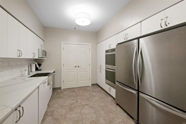 kitchen with white cabinetry, appliances with stainless steel finishes, backsplash, light stone countertops, and sink