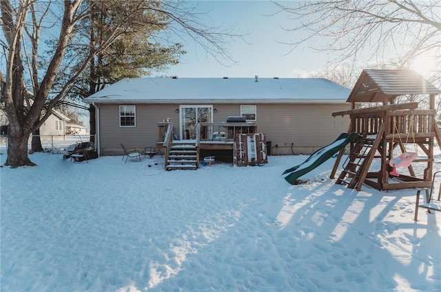 snow covered back of property featuring a playground and a deck