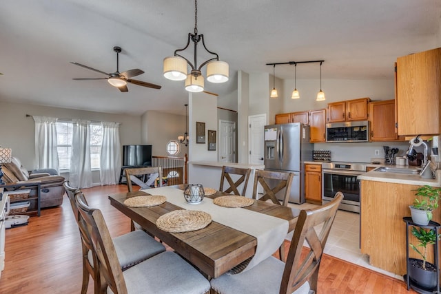 dining space with rail lighting, sink, vaulted ceiling, light hardwood / wood-style floors, and ceiling fan with notable chandelier