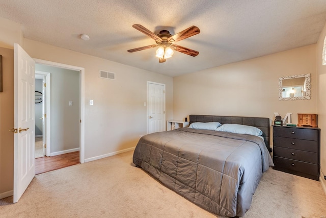 bedroom with ceiling fan, light colored carpet, and a textured ceiling