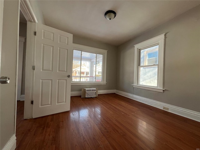 unfurnished bedroom featuring a wall mounted AC, dark hardwood / wood-style flooring, and multiple windows