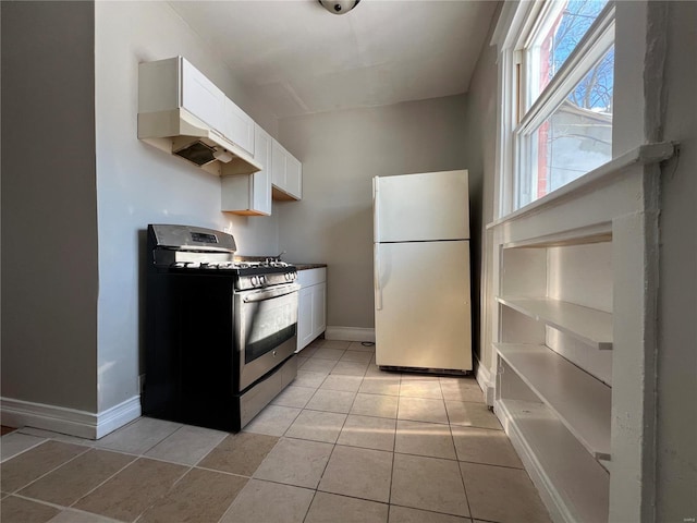 kitchen with gas stove, white cabinetry, light tile patterned floors, and fridge