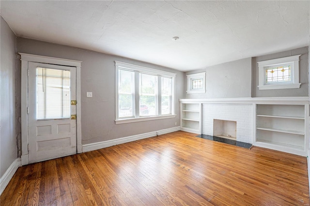 unfurnished living room with built in features, hardwood / wood-style flooring, and a brick fireplace