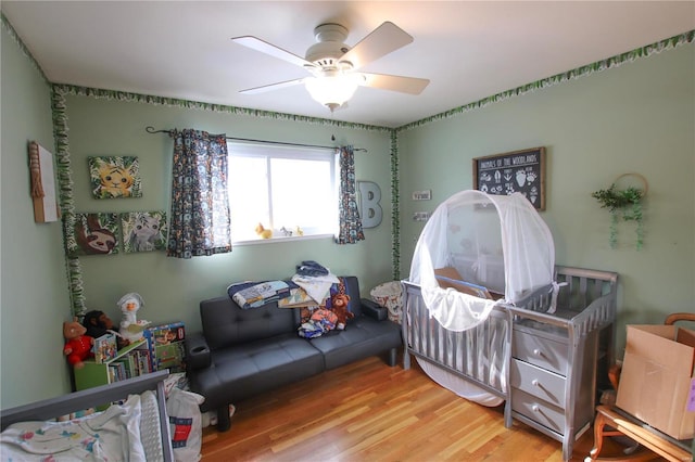 bedroom featuring light wood-type flooring, a nursery area, and ceiling fan