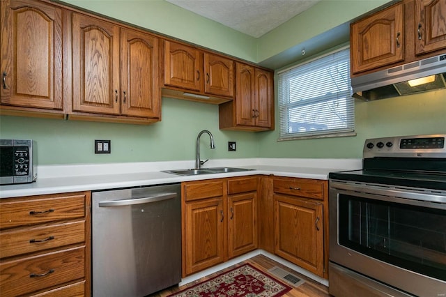 kitchen featuring ventilation hood, sink, a textured ceiling, appliances with stainless steel finishes, and light hardwood / wood-style floors