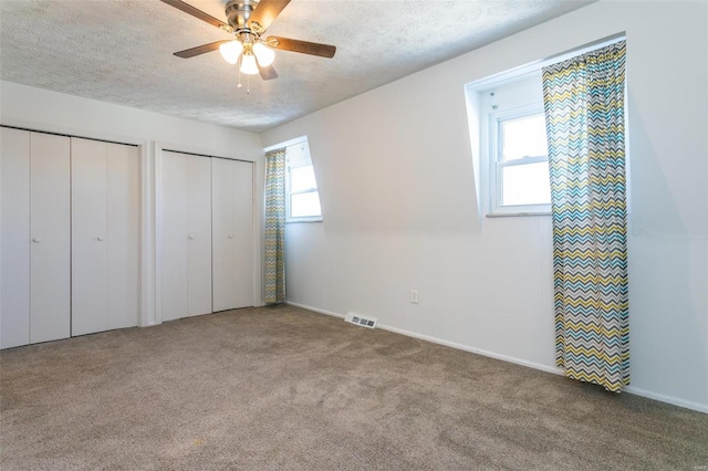 unfurnished bedroom with multiple closets, ceiling fan, carpet floors, and a textured ceiling