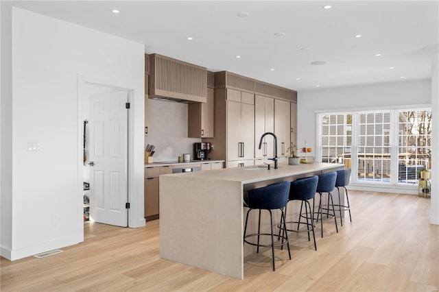 kitchen with an island with sink, light hardwood / wood-style floors, a kitchen breakfast bar, and sink