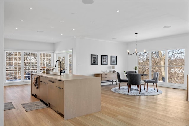 kitchen featuring decorative light fixtures, an island with sink, a notable chandelier, light hardwood / wood-style floors, and sink