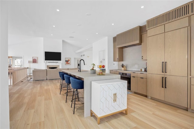 kitchen featuring light hardwood / wood-style flooring, an island with sink, stainless steel oven, and wall chimney exhaust hood