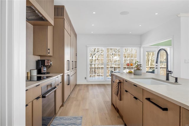 kitchen with light hardwood / wood-style floors, black electric stovetop, light brown cabinetry, sink, and oven