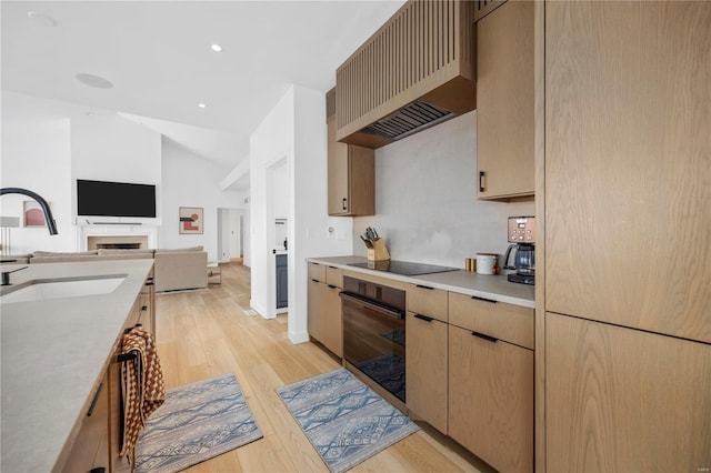 kitchen featuring sink, vaulted ceiling, custom range hood, light hardwood / wood-style flooring, and black appliances