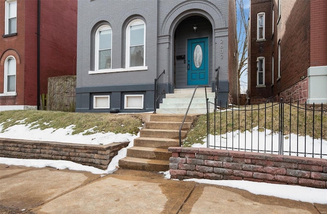 snow covered property entrance featuring brick siding and fence