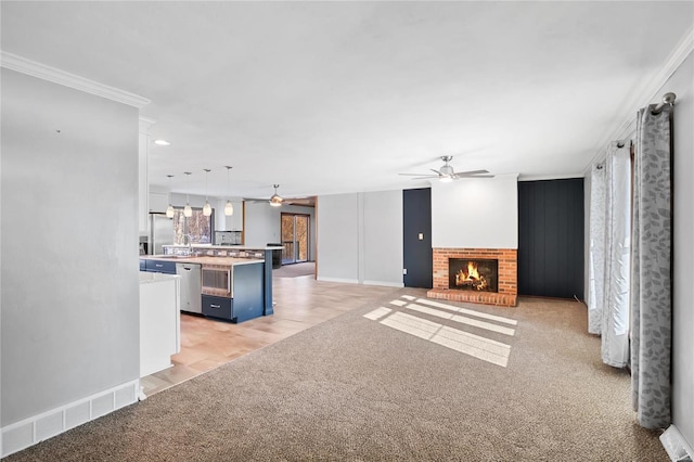 unfurnished living room featuring ornamental molding, light colored carpet, a fireplace, and ceiling fan