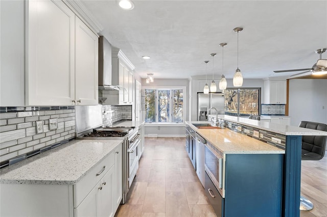 kitchen with stainless steel appliances, white cabinetry, and wall chimney range hood