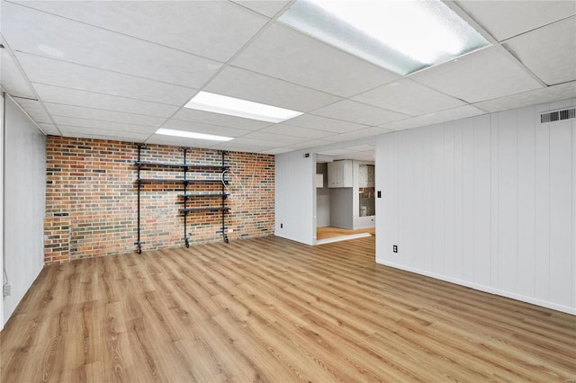 basement with brick wall, a drop ceiling, and light hardwood / wood-style flooring