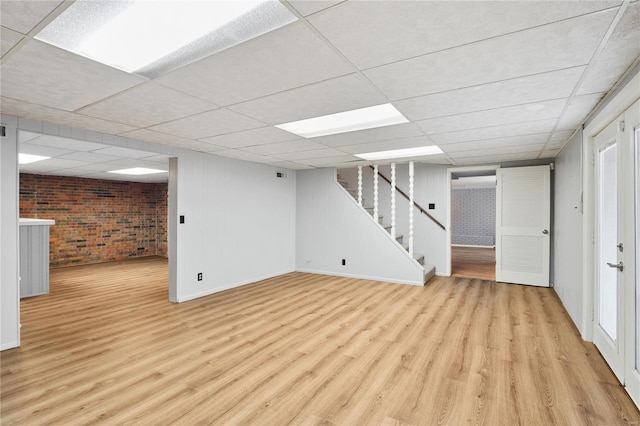 basement with light hardwood / wood-style floors, brick wall, and a drop ceiling