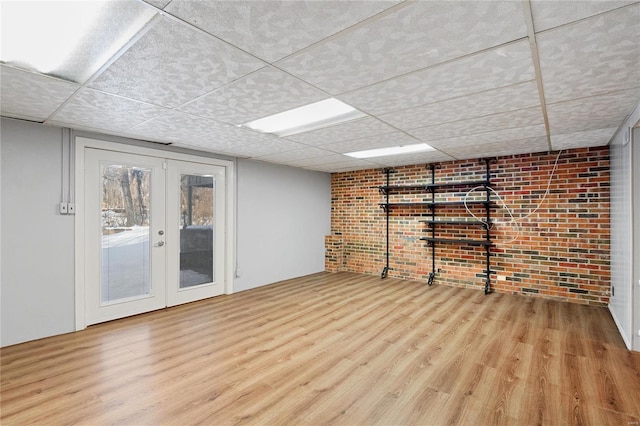 basement with light hardwood / wood-style flooring, french doors, and brick wall