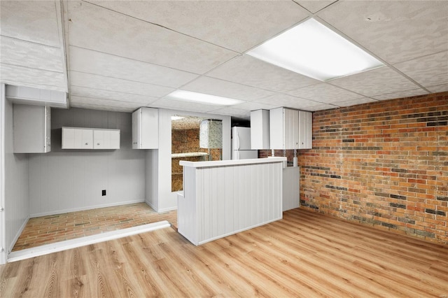 kitchen with kitchen peninsula, a paneled ceiling, brick wall, white cabinetry, and white refrigerator