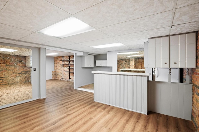 kitchen featuring brick wall, light wood-type flooring, a paneled ceiling, and white cabinetry