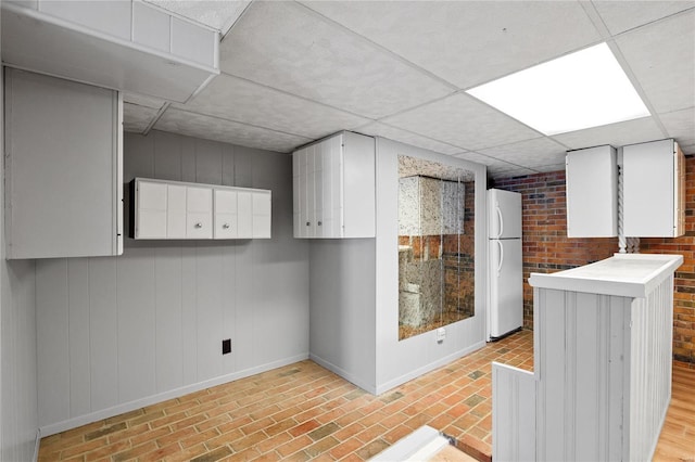 basement featuring white refrigerator and a drop ceiling