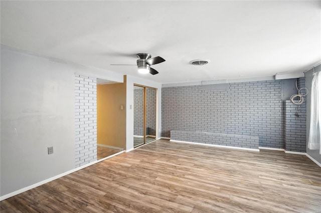 unfurnished bedroom featuring ceiling fan, a closet, brick wall, and hardwood / wood-style flooring