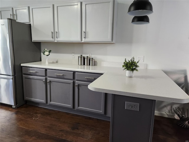 kitchen featuring kitchen peninsula, gray cabinets, dark hardwood / wood-style flooring, stainless steel refrigerator, and pendant lighting