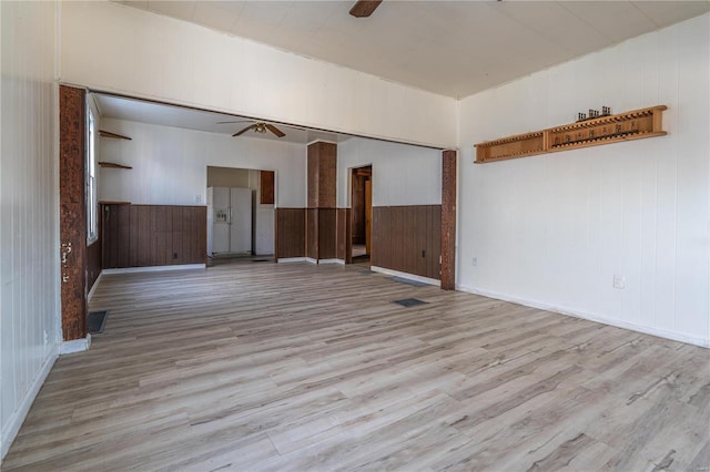 empty room featuring ceiling fan, light hardwood / wood-style flooring, and wooden walls