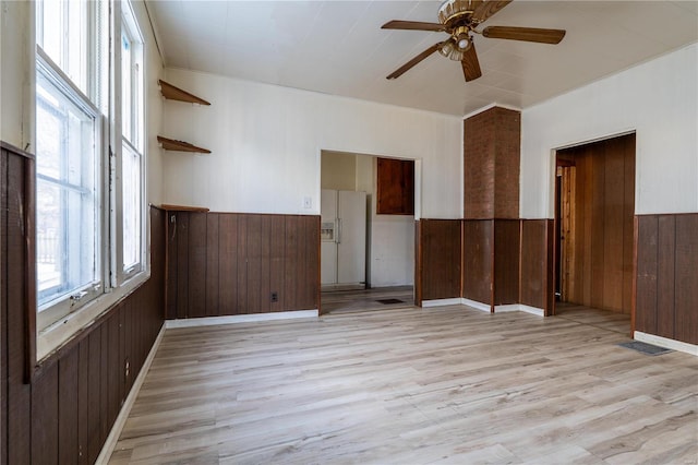 spare room with ceiling fan, wood walls, and light hardwood / wood-style flooring