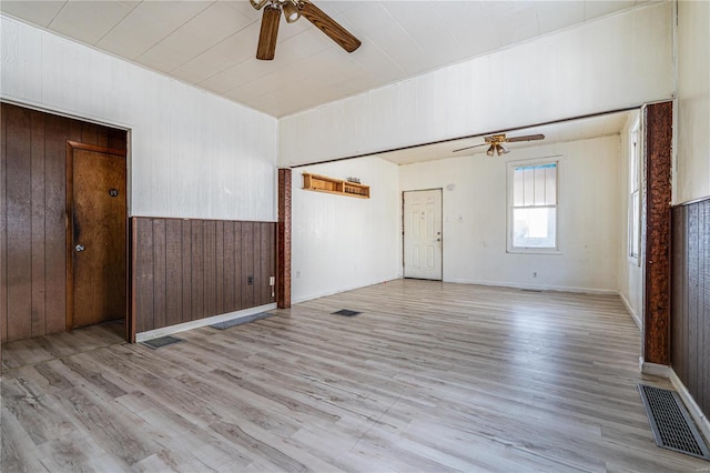 spare room with ceiling fan, light wood-type flooring, and wooden walls