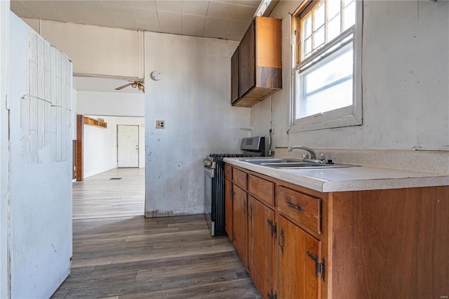 kitchen featuring ceiling fan, stainless steel gas range oven, sink, and dark hardwood / wood-style flooring