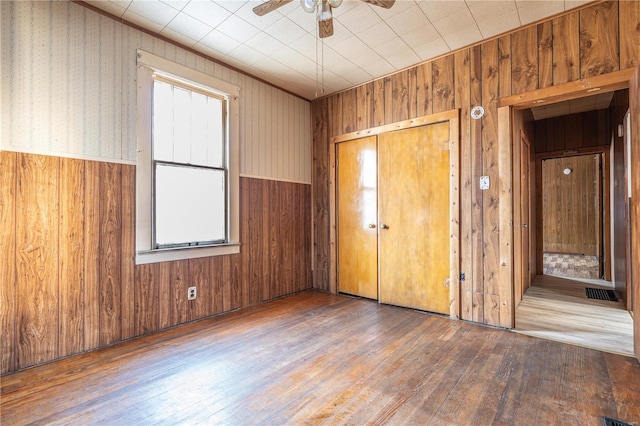 unfurnished bedroom with ceiling fan, hardwood / wood-style floors, a closet, and wooden walls