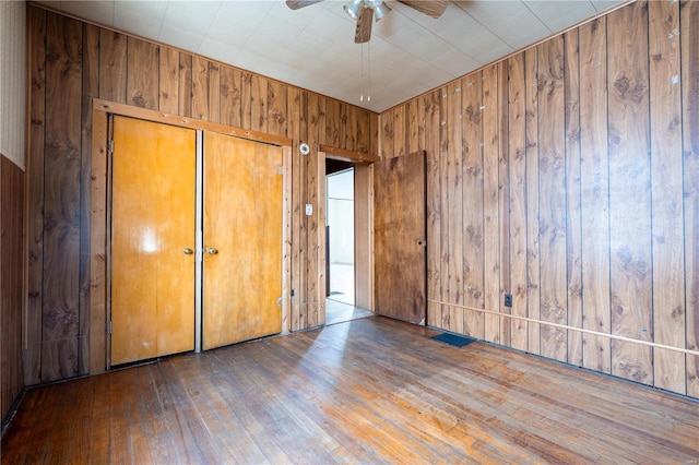 unfurnished bedroom with ceiling fan, dark hardwood / wood-style floors, a closet, and wooden walls