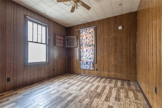 unfurnished room featuring ceiling fan, light hardwood / wood-style floors, and wooden walls