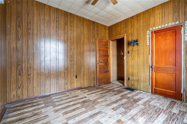 empty room featuring ceiling fan, light hardwood / wood-style flooring, and wooden walls