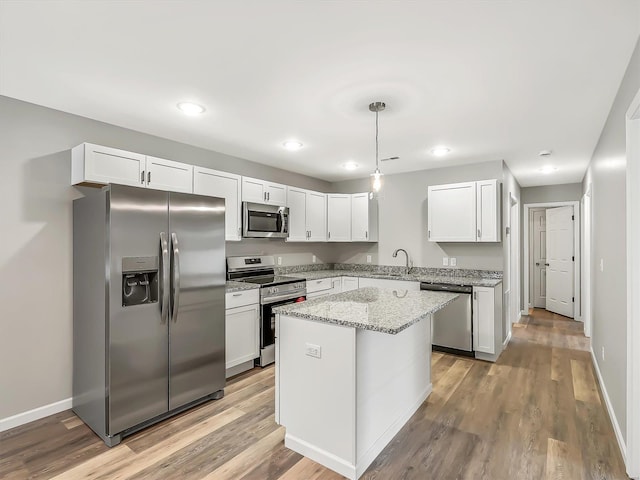 kitchen featuring white cabinets, hanging light fixtures, light stone countertops, a kitchen island, and stainless steel appliances