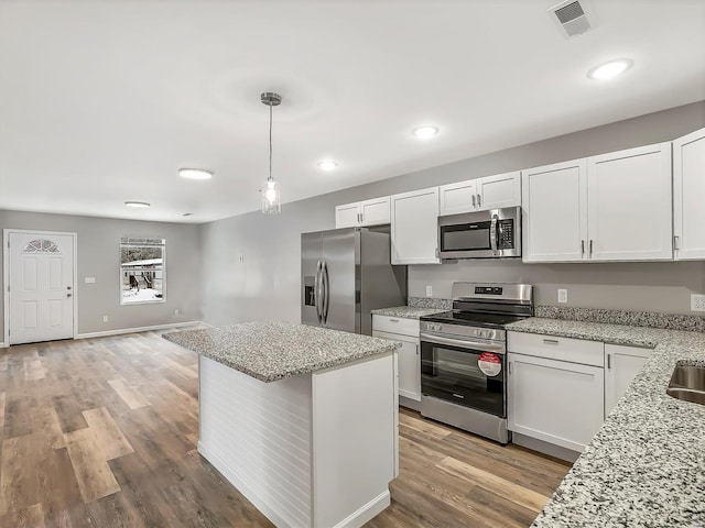 kitchen with appliances with stainless steel finishes, white cabinetry, hanging light fixtures, and light stone counters