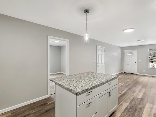 kitchen featuring light wood-type flooring, light stone counters, decorative light fixtures, a center island, and white cabinetry