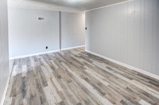 spare room featuring wood walls, light hardwood / wood-style flooring, and a textured ceiling