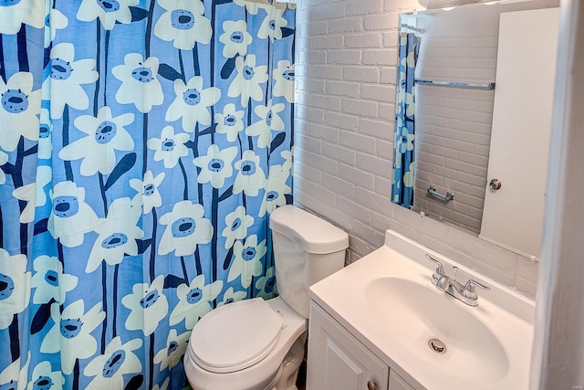 bathroom with vanity, toilet, and brick wall