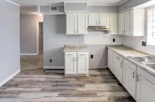 kitchen with white cabinetry, light stone countertops, sink, light hardwood / wood-style flooring, and ornamental molding