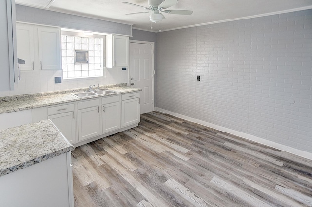 kitchen with light wood-type flooring, ornamental molding, brick wall, sink, and white cabinetry