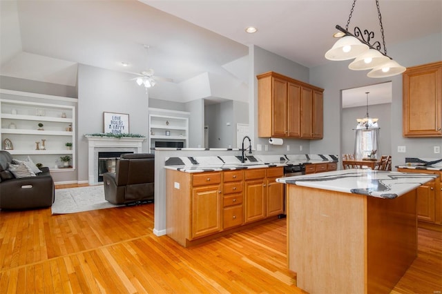 kitchen with light wood-type flooring, decorative light fixtures, built in features, a premium fireplace, and a kitchen island